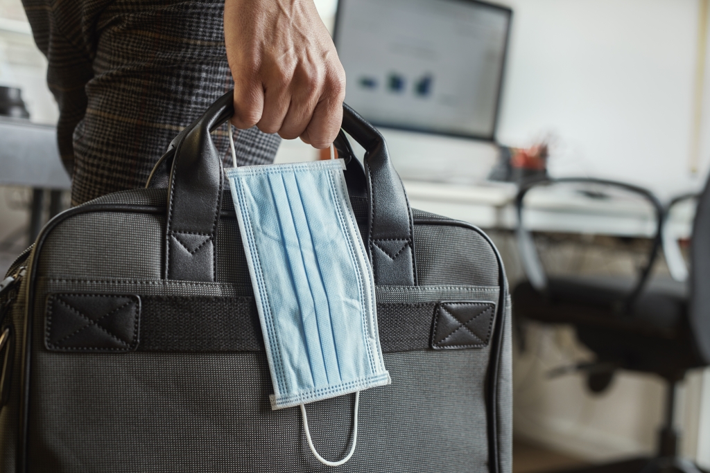 close up of person holding black suit case with blue medical mask