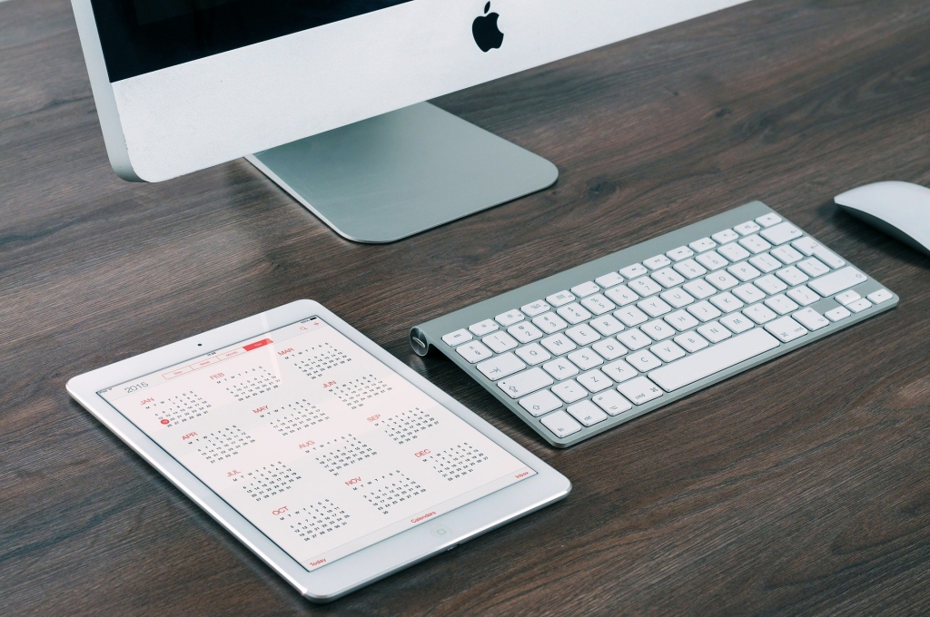 laptop sitting on desk with ipad beside it. The ipad has a calendar showing